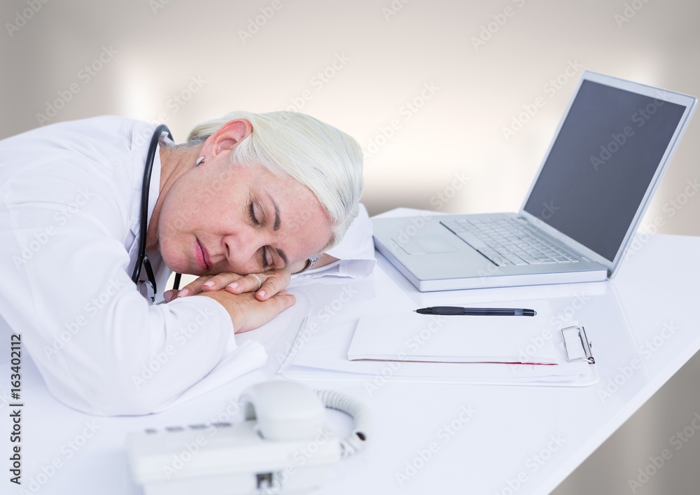 Doctor asleep at desk against white blurred hallway