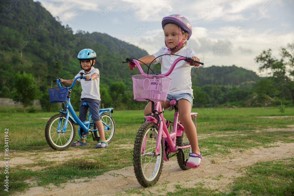 Two child riding a bicycle. The kids in a helmet riding a bike in the park. Beautiful kids.