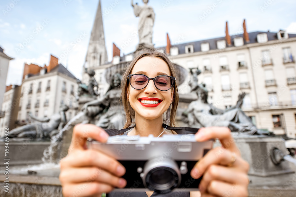 Young and happy woman tourist with photo camera standing near the fountain on the Royal square in Na