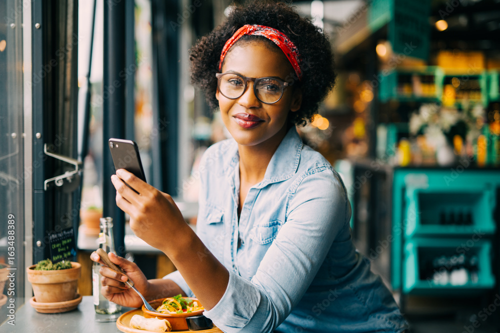 Smiling young African woman working online by a cafe window