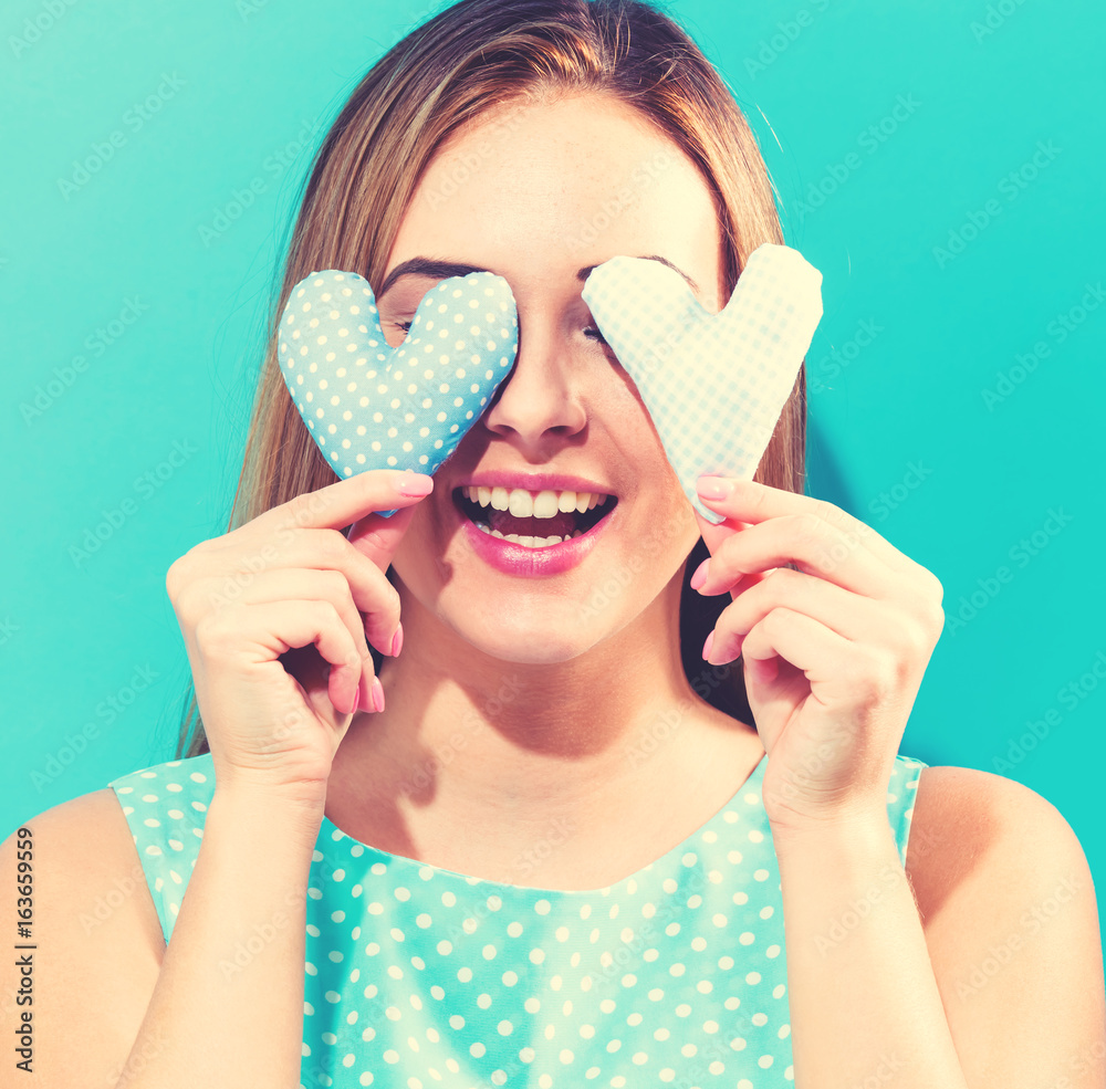 Happy young woman holding heart cushions on a blue background