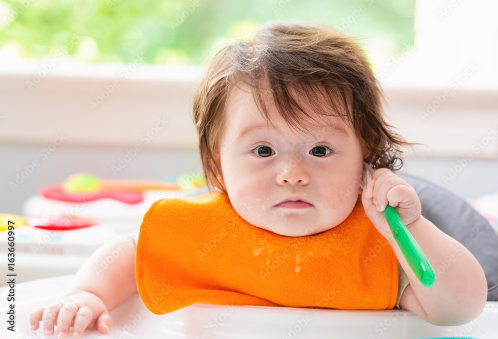 Happy little baby boy eating food with a spoon