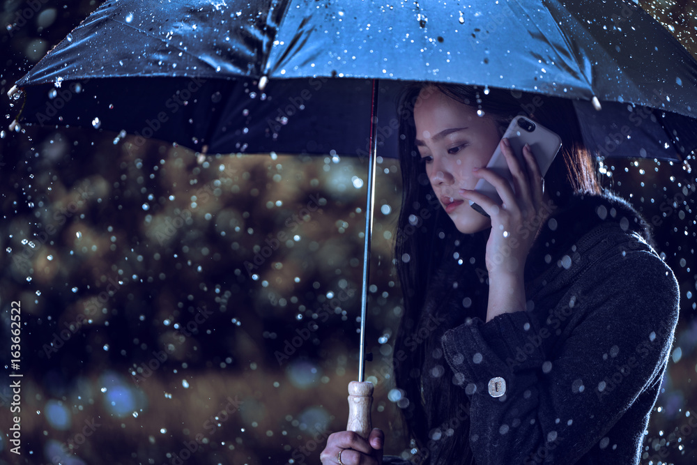 亚洲妇女正在打伞，雨正在下。她在打电话