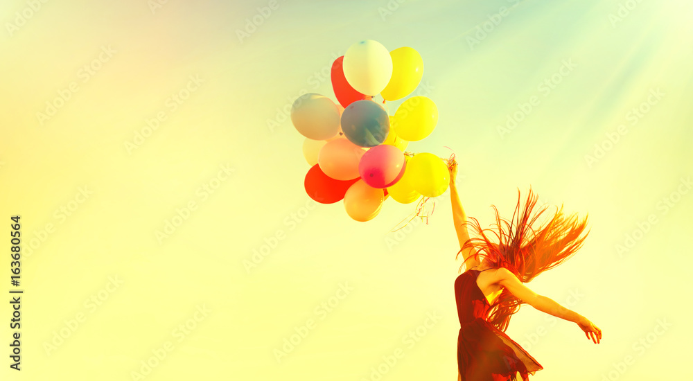 Beauty girl running and jumping on summer field with colorful air balloons over clear sky