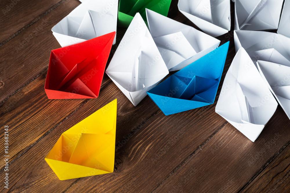 Business leadership concept with white and color paper boats on wooden table