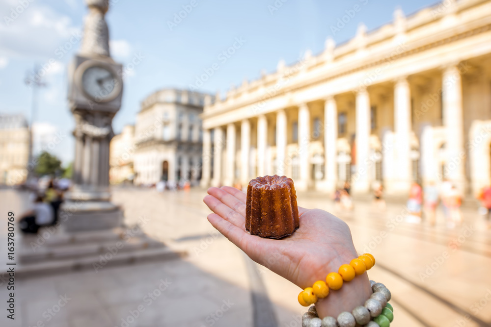 Holding a traditional Bordeaux sweet cake called Canele outdoors on the street near the Grand theatr