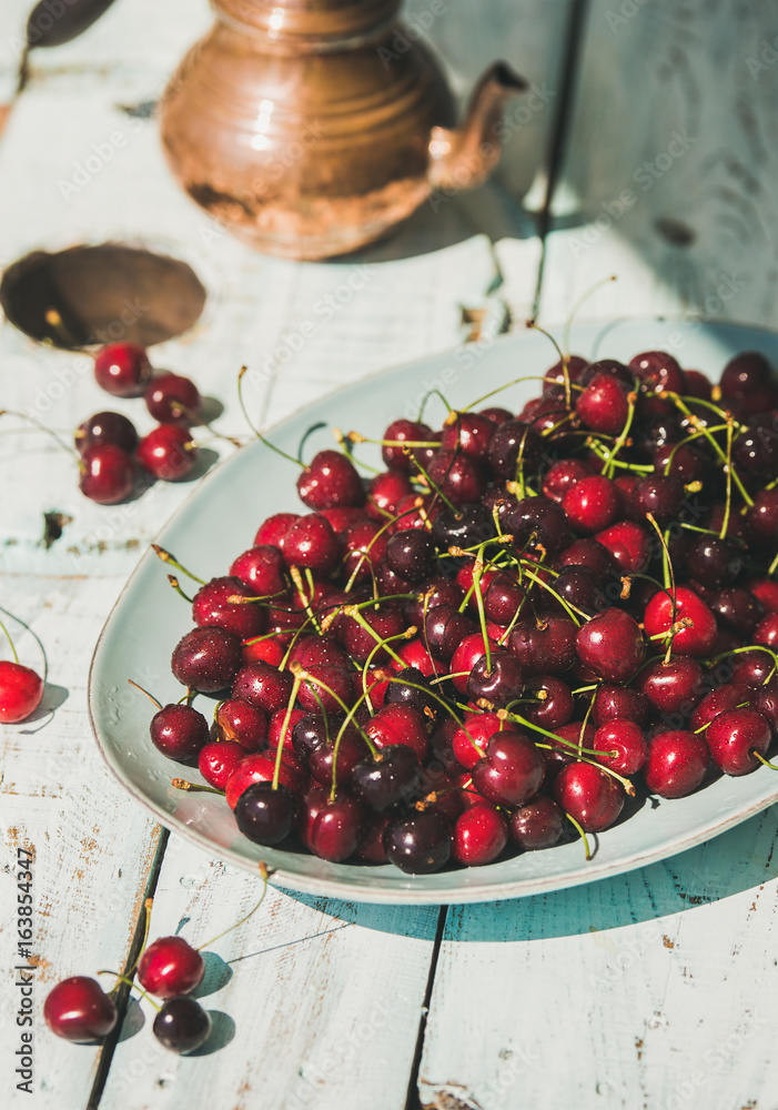 Plate of fresh ripe sweet cherries on rustic light blue wooden garden table, selective focus, vertic