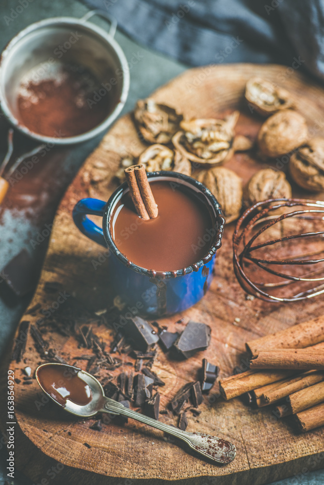 Rich winter hot chocolate with cinnamon sticks and walnuts in blue enamel mug on rustic wooden board