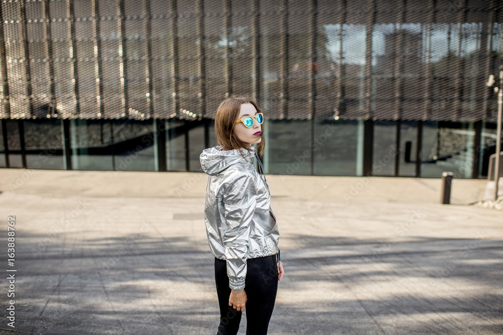 Lifestyle portrait of a stylish woman in silver jacket walking outdoors in the modern urban environm