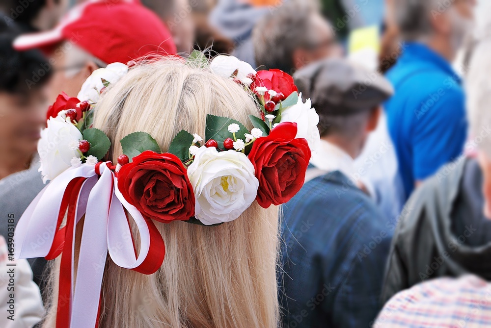 Young woman in roses wreath standing and hiding bouquet of flowers behind her back. Blurred. backgro