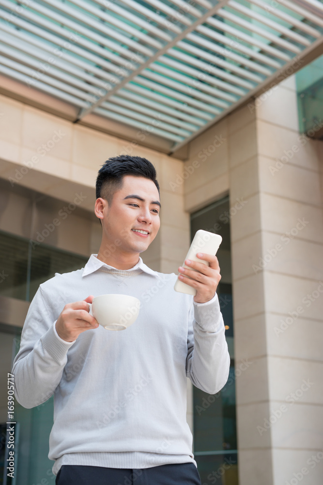 英俊的年轻人在城市喝咖啡并使用手机