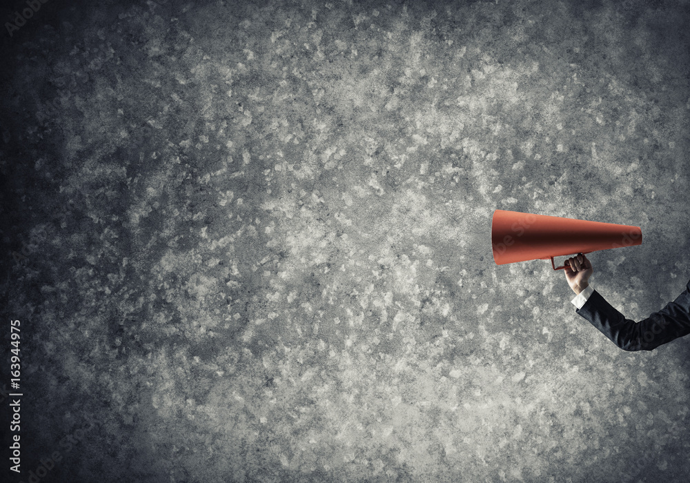 Hand of businesswoman holding red paper trumpet against concrete background