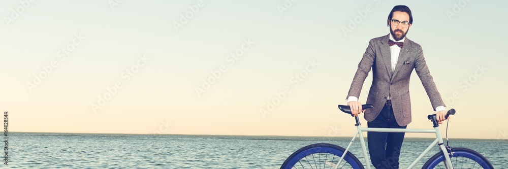 Millennial man with bow tie and bicycle against horizon