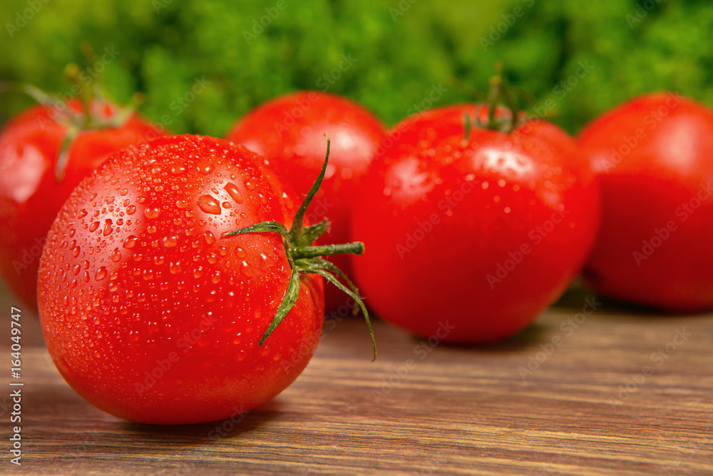 Fresh ripe tomatoes on a wooden table with a green salad on the background. Fresh vegetables.