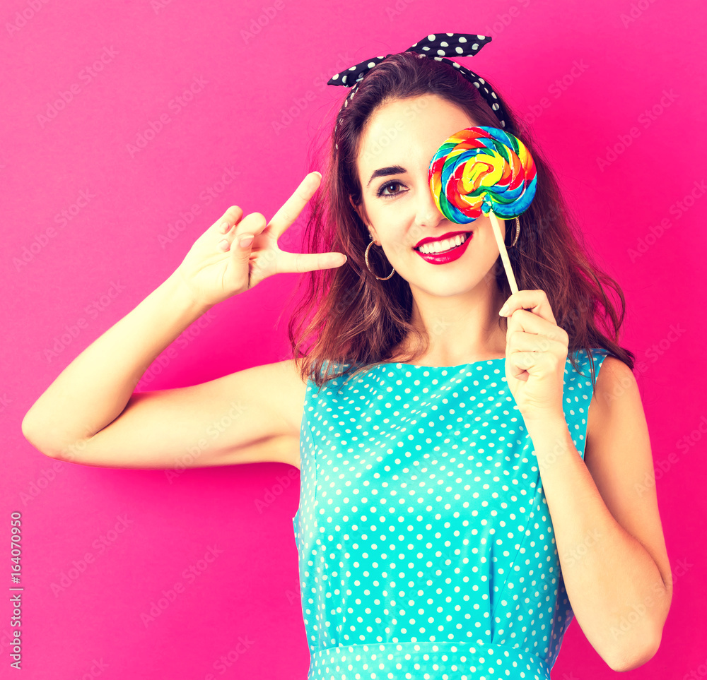 Young woman holding a lollipop on a pink background