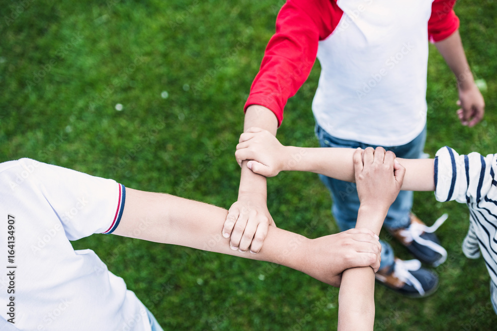 Close-up partial view of children holding hands while standing on green lawn in park