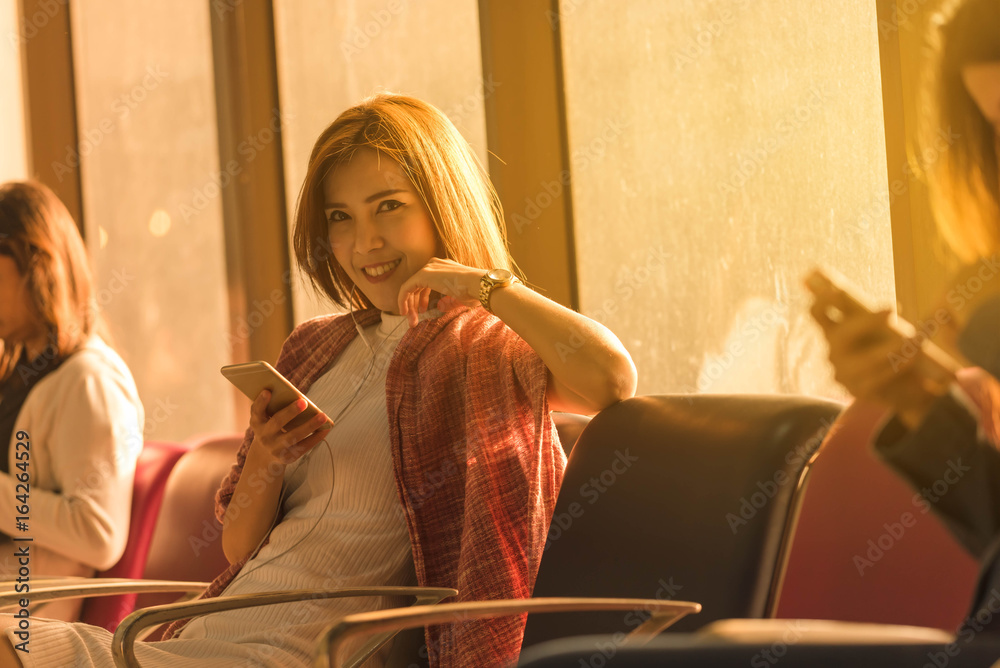 Young beautiful woman sit in airport with travel bag use smartphone with ear phone at airport wait f