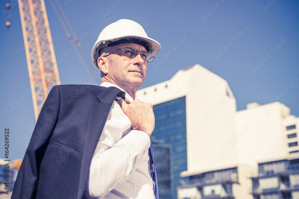 Senior elegant builder man in suit at construction site on sunny