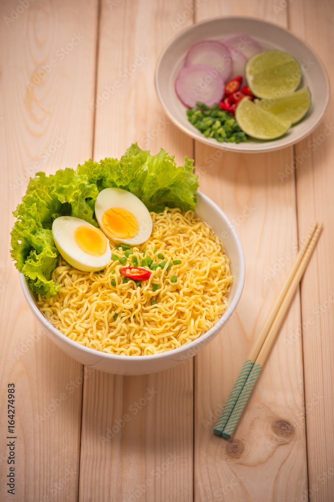 Instant noodles in bowl with vegetables and  boiled egg on wood background