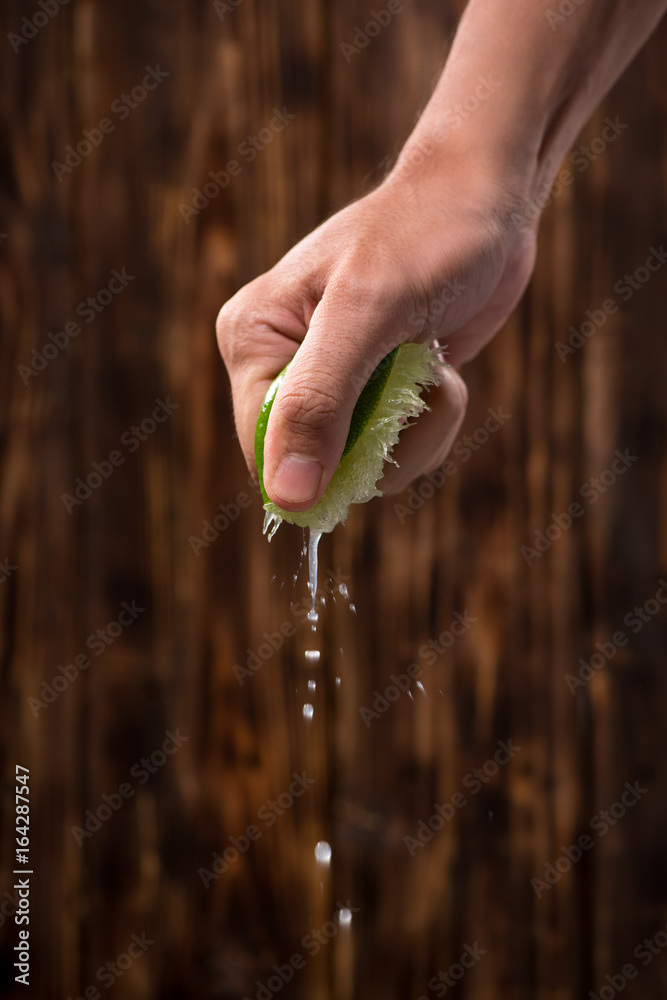 Hand squeeze lime with lime drop on dark wooden background