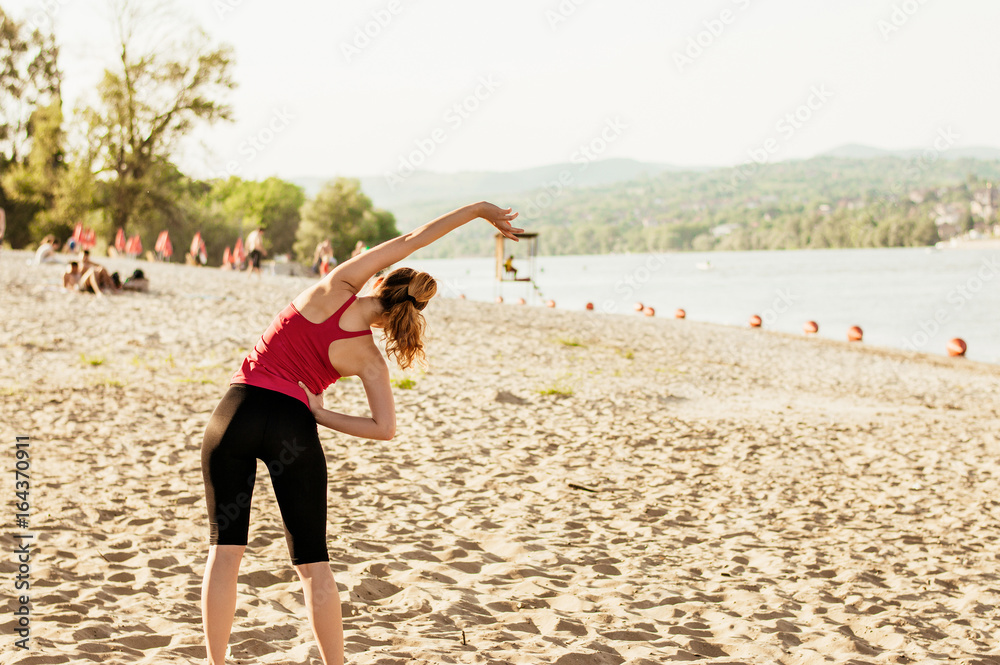 Sporty woman doing body stretching at the beach, back view.