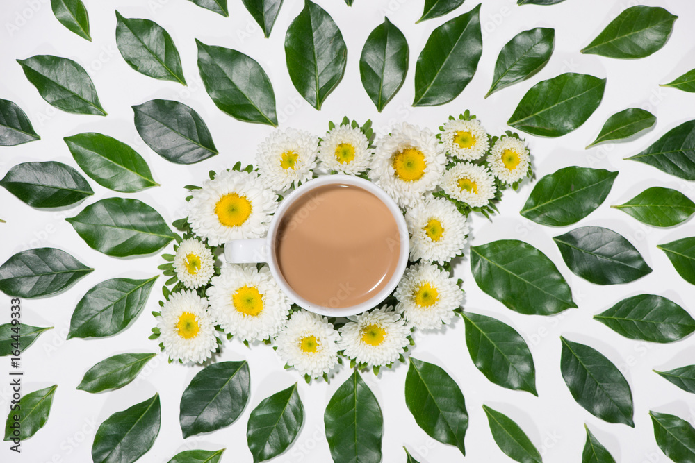 Flat lay of green leaves and flowers pattern with cup of coffee on white background