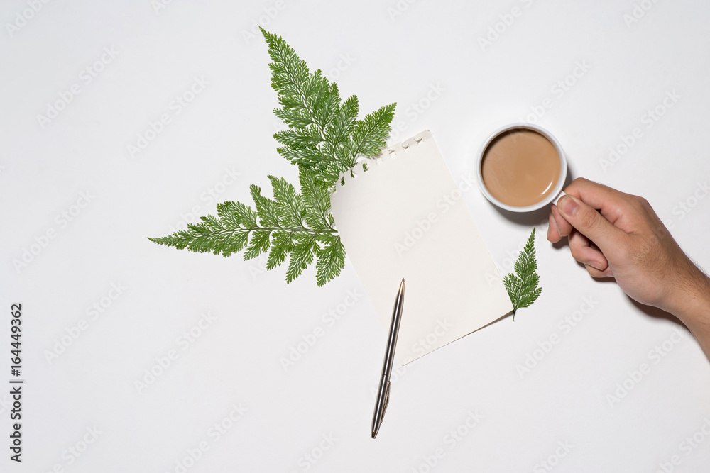 Flat lay of green leaves and flowers pattern with cup of coffee and paper note on white background