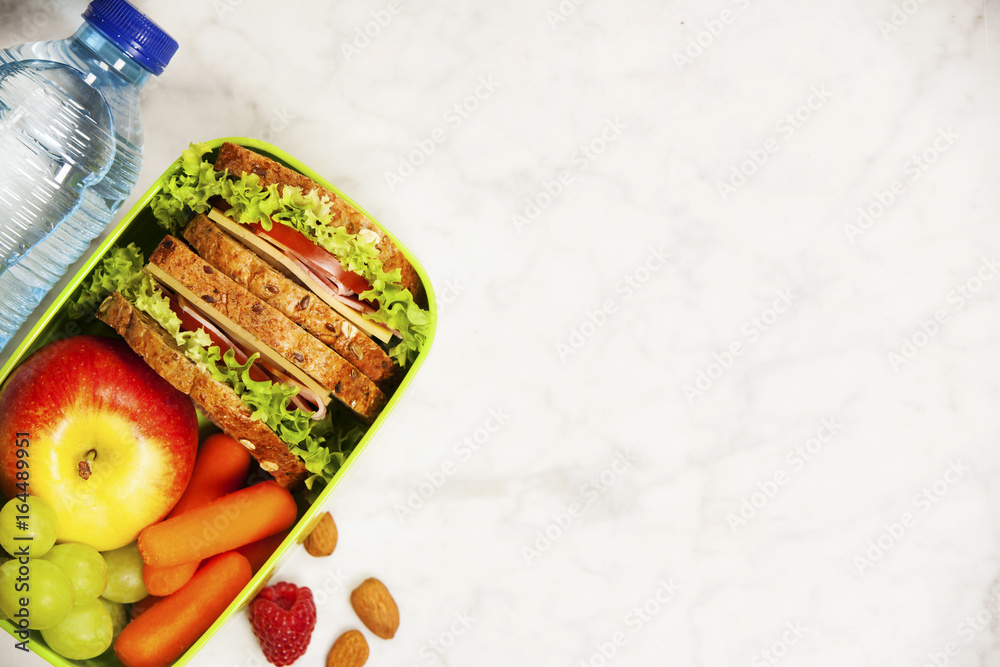 Green school lunch box with sandwich, apple, grape, carrot and bottle of water