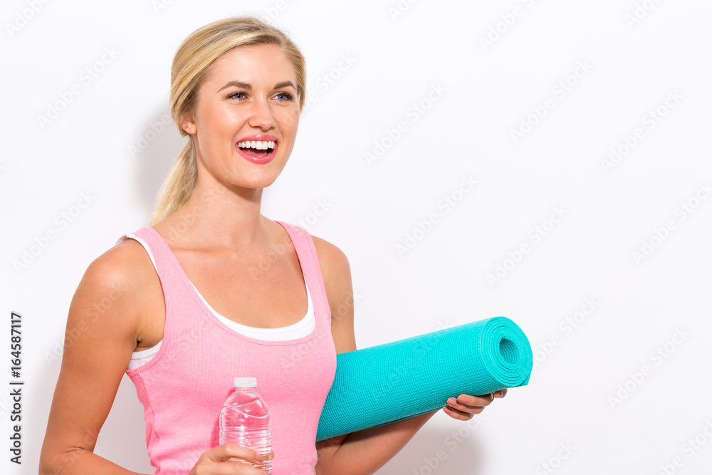 Happy young woman holding a yoga mat and a water bottle 