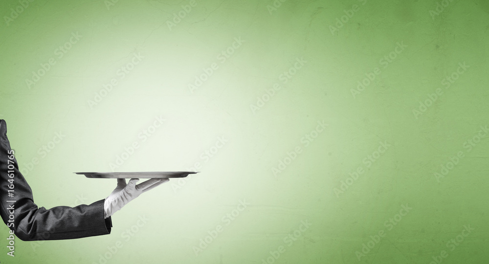 Hand of butler holding empty metal tray against green background