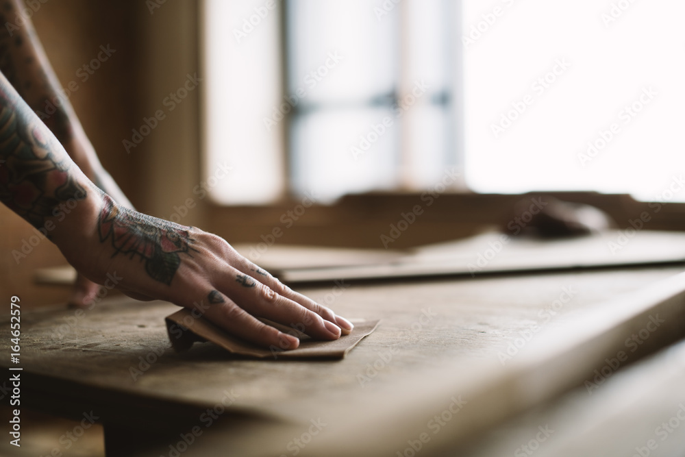 Hands with tattoo using sandpaper on a wood