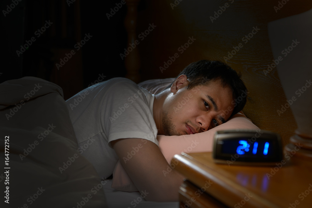 Depressed man suffering from insomnia lying in bed