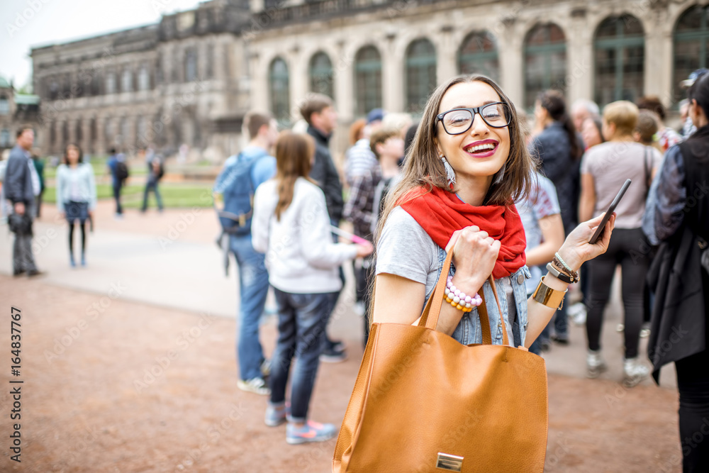 Young smiling woman photographing with smartphone while visiting with tourist group the old palace i