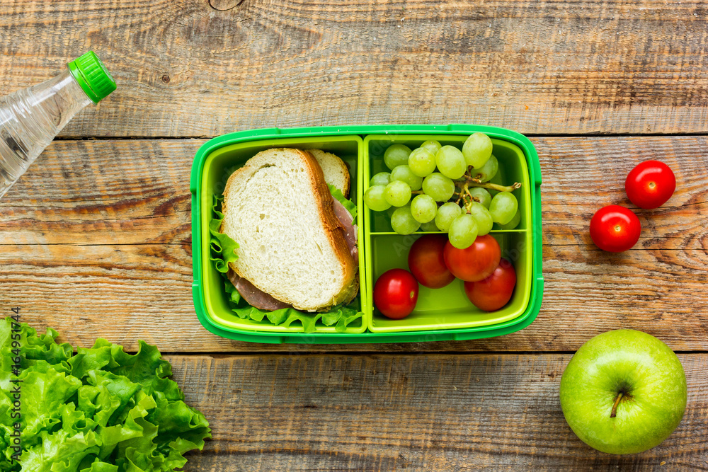 homemade lunch with apple, grape and sandwich in green lunchbox top view