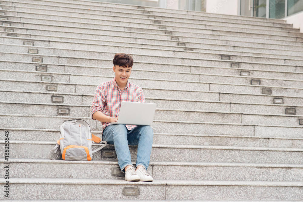 Handsome student in shirt working on laptop sitting on stairs in college