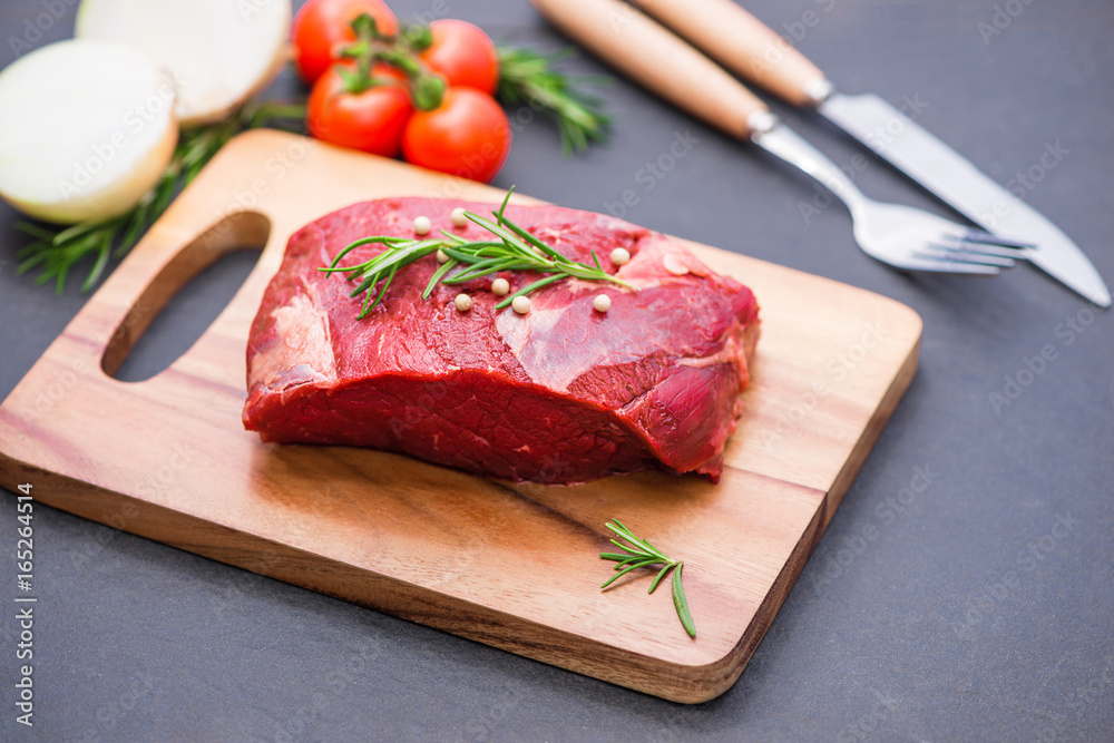 Raw beef on a cutting board  with spices and ingredients for cooking.