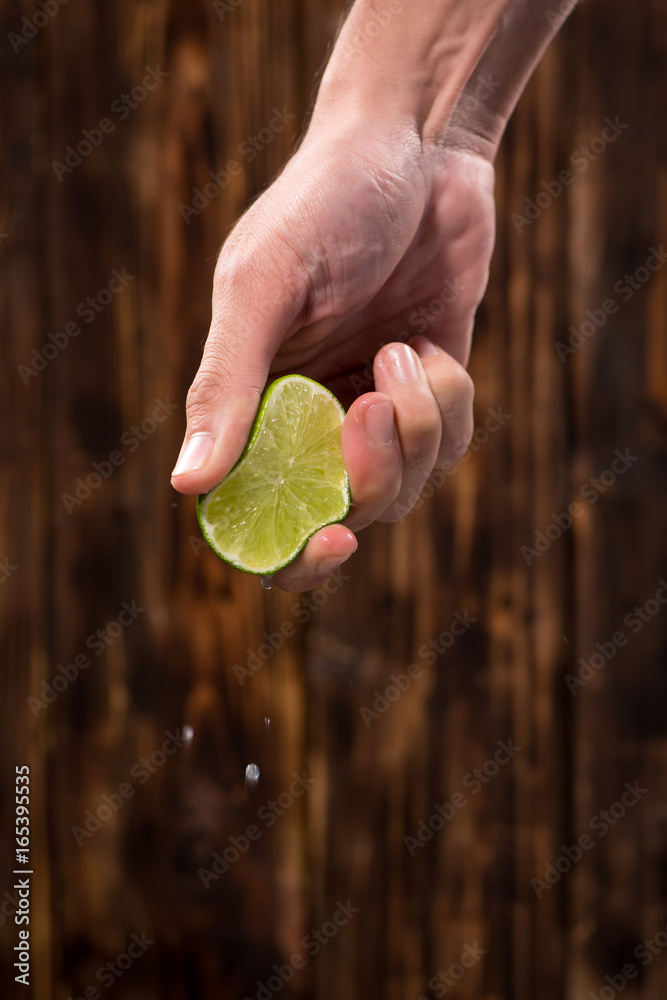 Hand squeeze lime with lime drop on dark wooden background