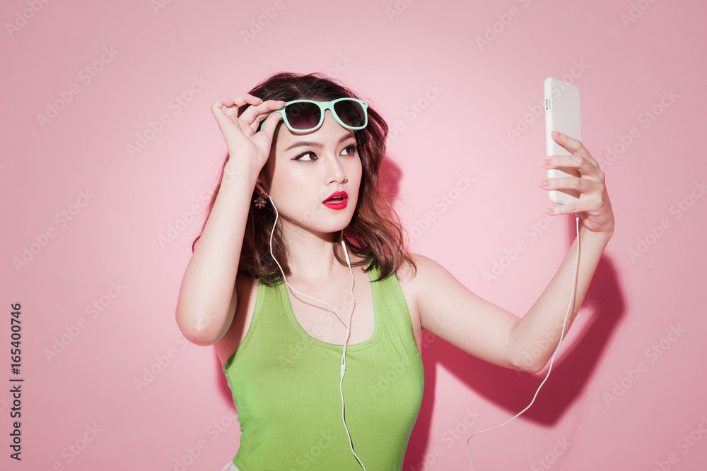 Stylish asian woman taking selfie photo on pink background.