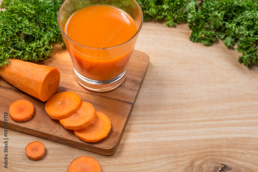 Glass of fresh carrot juice with vegetables on wooden table.