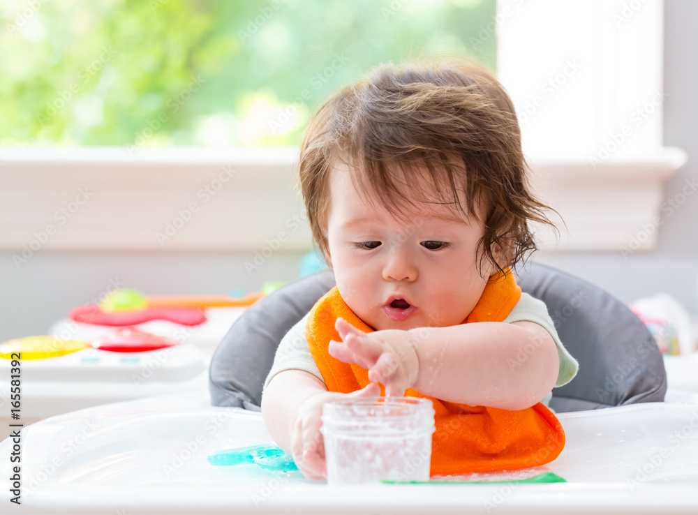 Happy little baby boy eating food from a jar