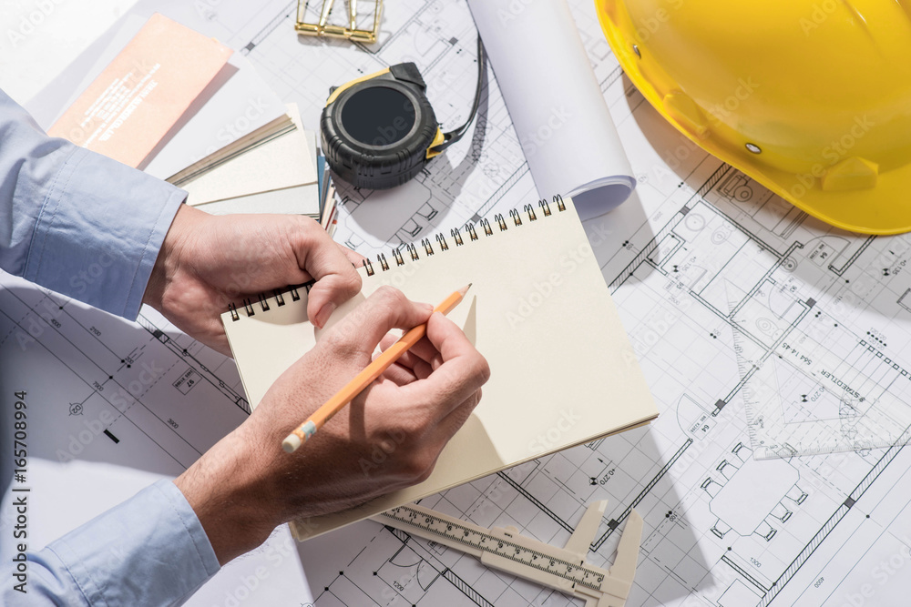 Working on blueprints. Construction project with hands writing on notebook.