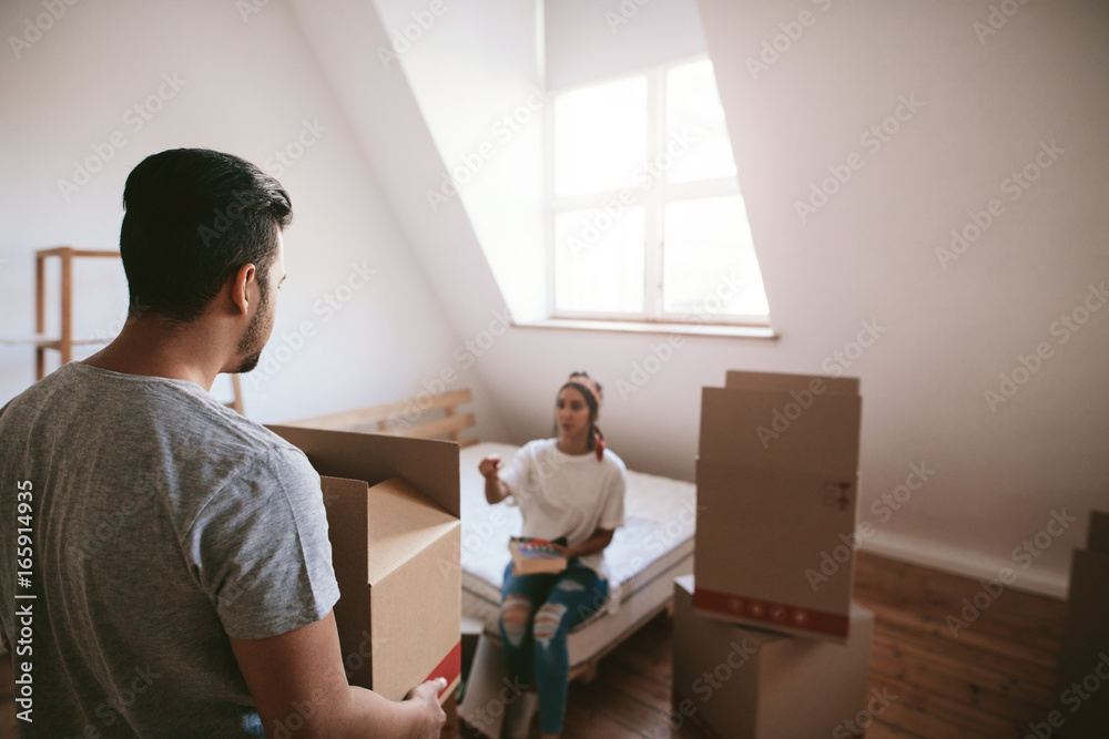 Young man carrying box with woman in background in new house