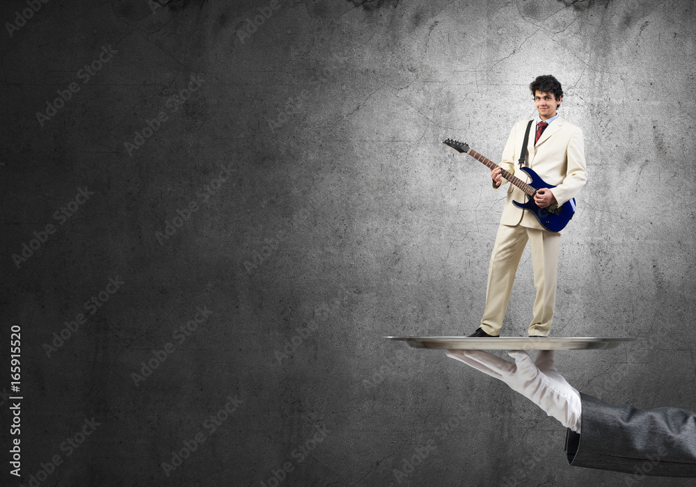 Businessman on metal tray playing electric guitar against concrete background