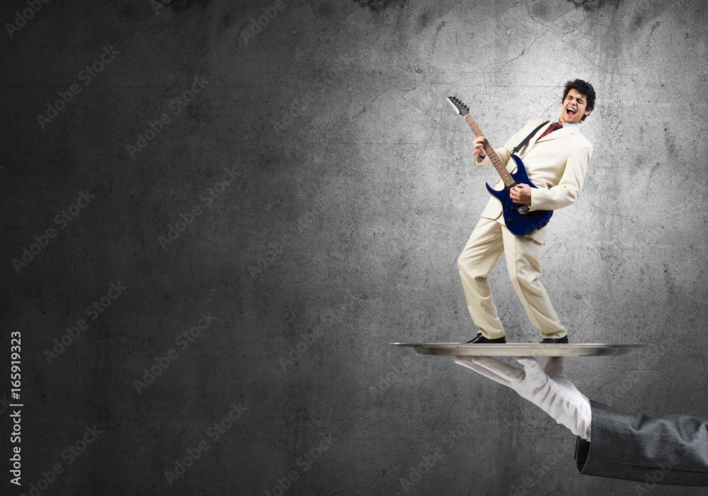 Businessman on metal tray playing electric guitar against concrete background