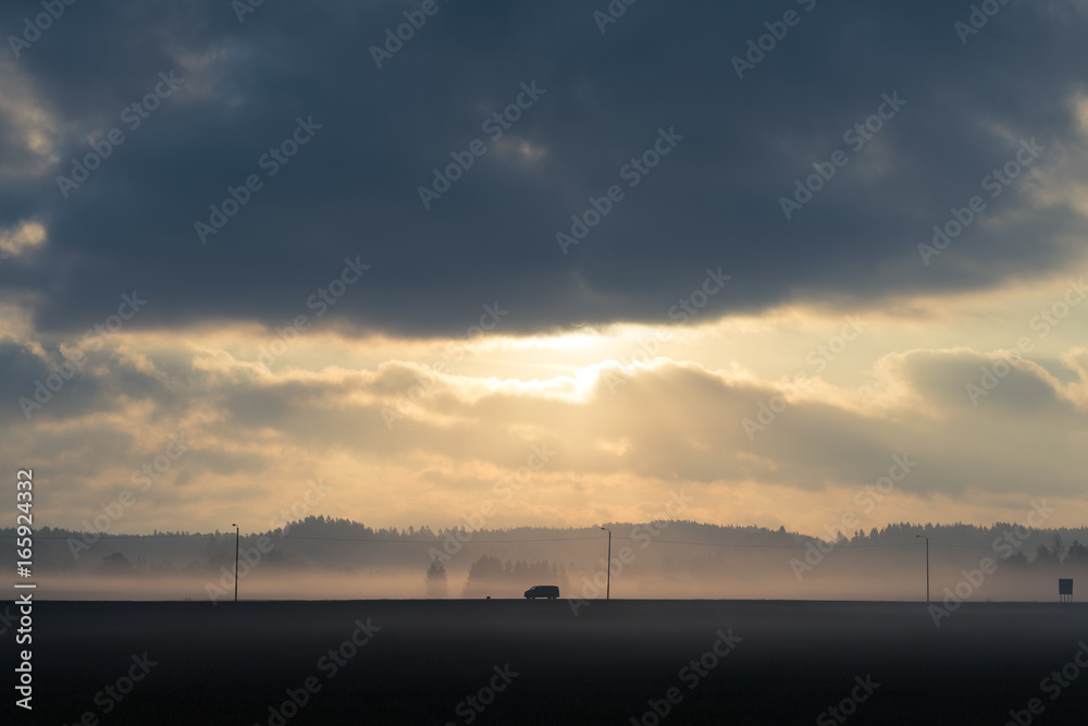 Single car driving through misty landscape with dramatic clouds and light