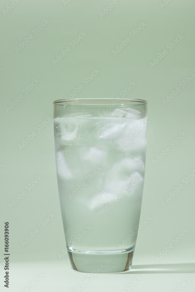 Ice drinking water glass on table over green.