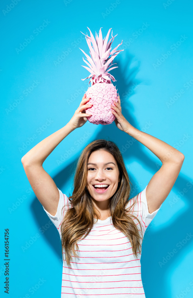 Happy young woman holding a pineapple on blue background