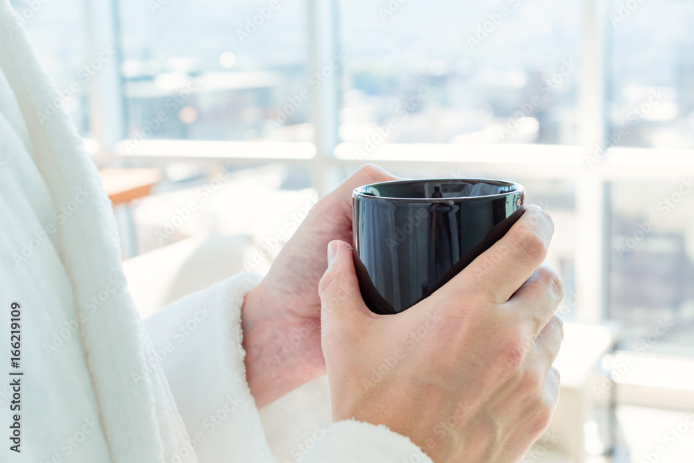 Man in a bathrobe with a cup of coffee in a brightly lit modern interior living space