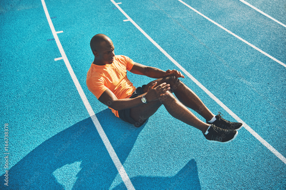 Fit young athlete doing crunches on a running track