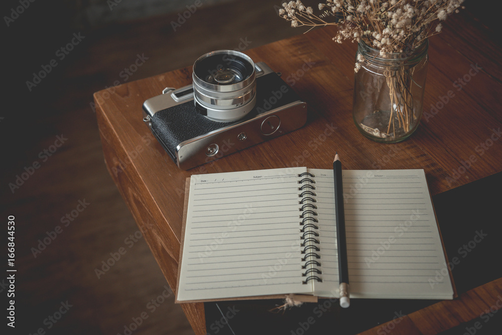 Notebook and classic camera on wood table with dry flower in vase,vintage filter